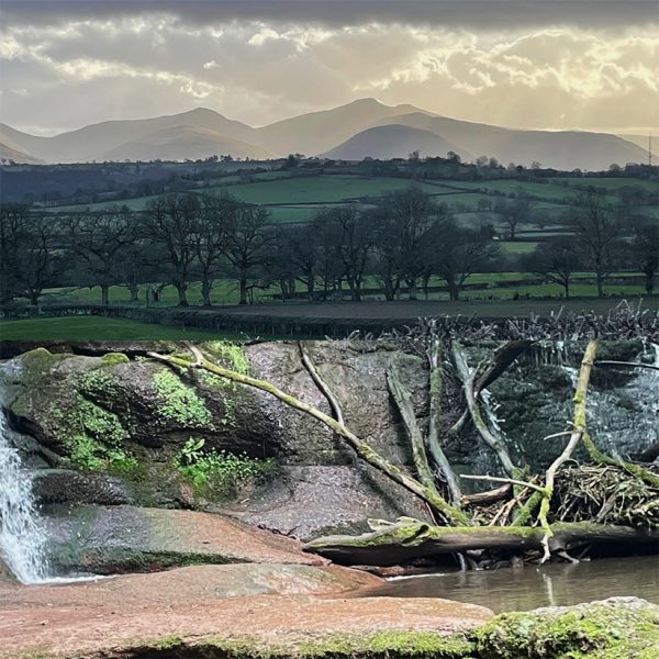 Photomontage Black Mountains waterfall in the foreground and Brecon Beacons in distance. Stormy skies